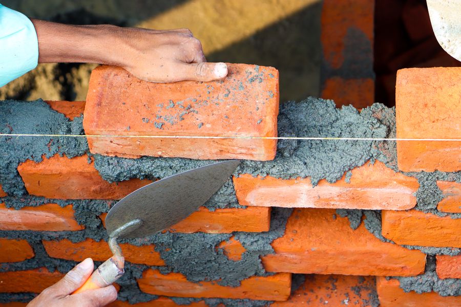 Bricklayer's hands laying red bricks and mortar with a trowel