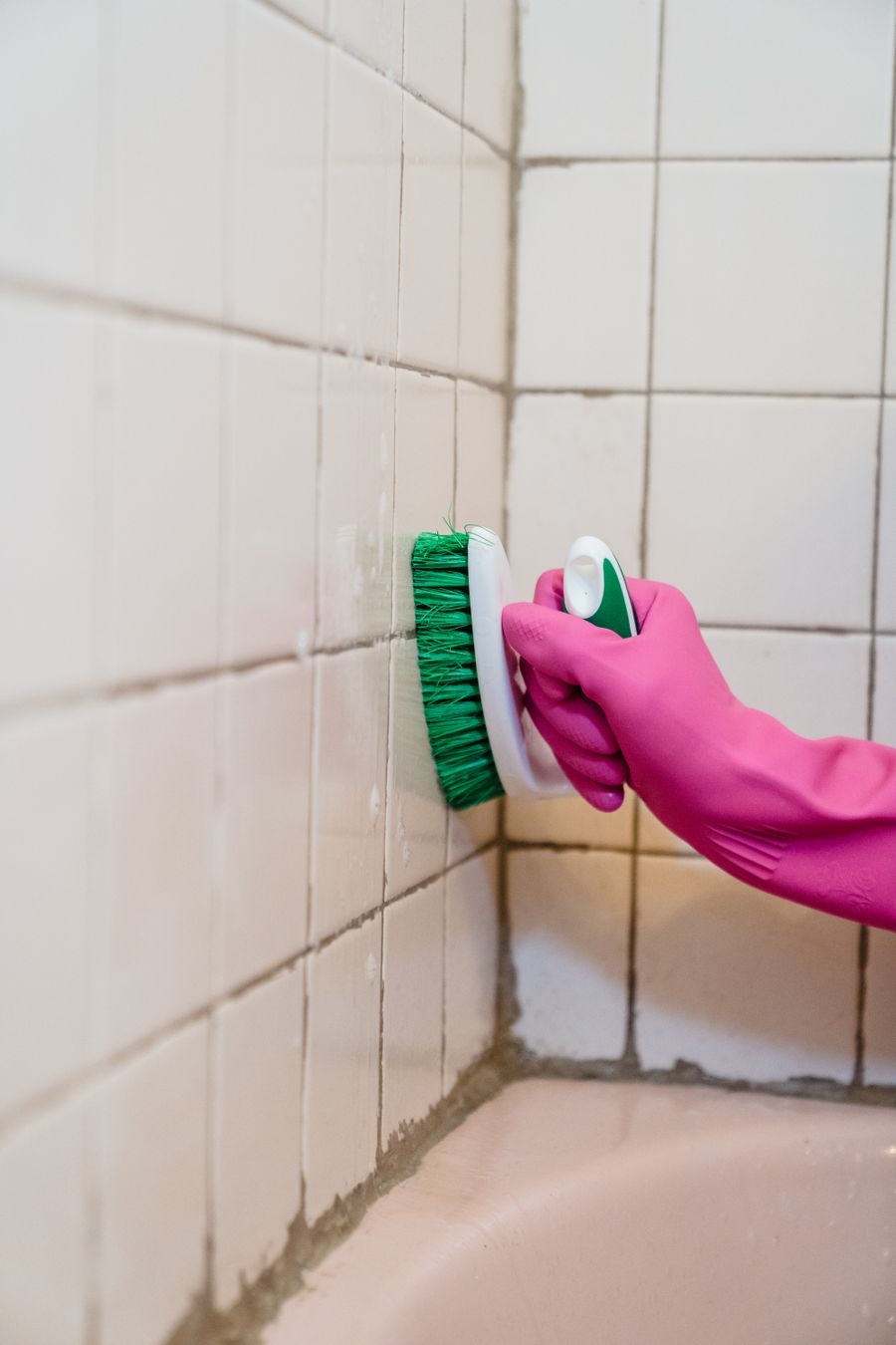 A rubber-gloved hand scrubbing bathroom tiles with a brush