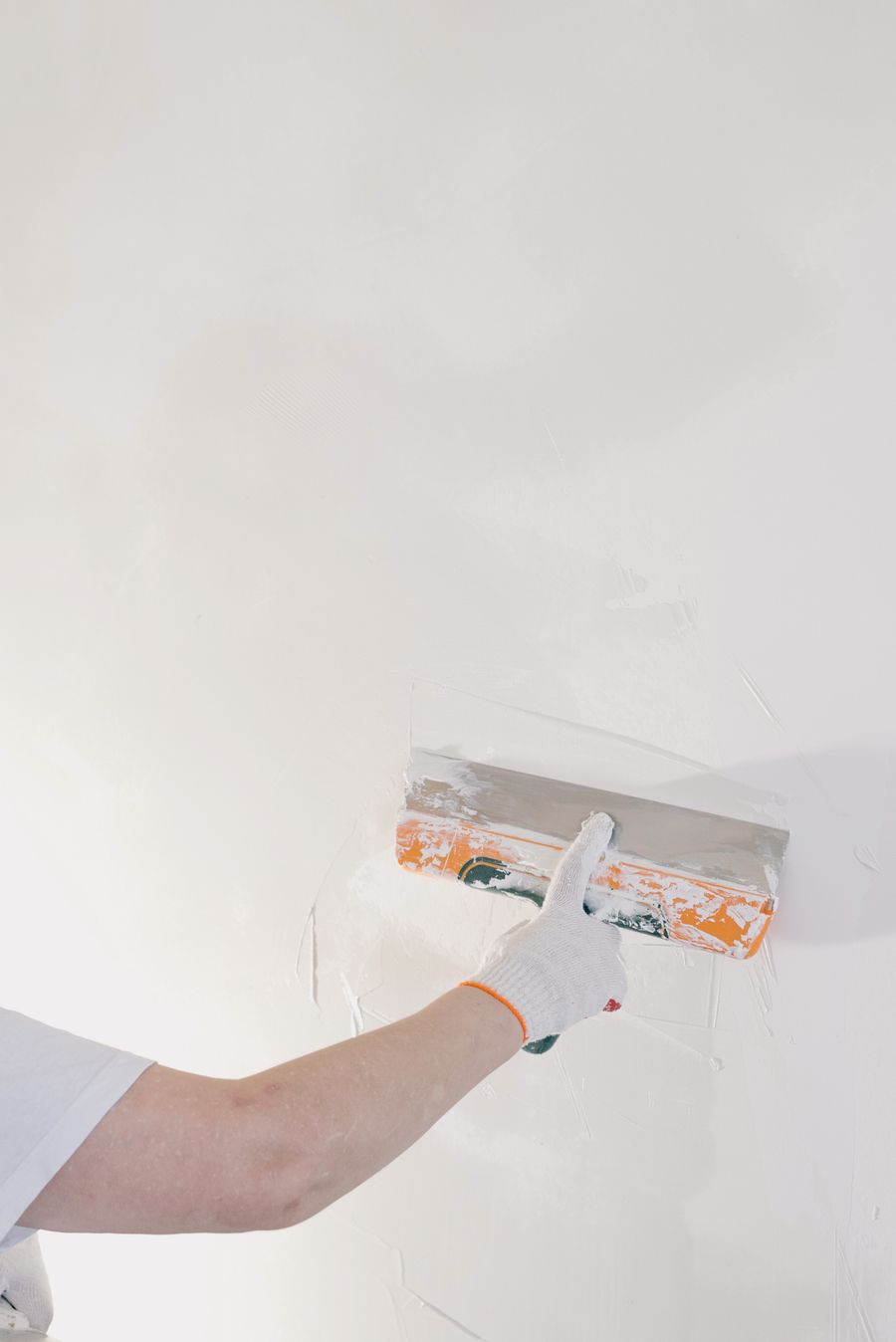 A gloved hand smoothing plaster on an interior wall