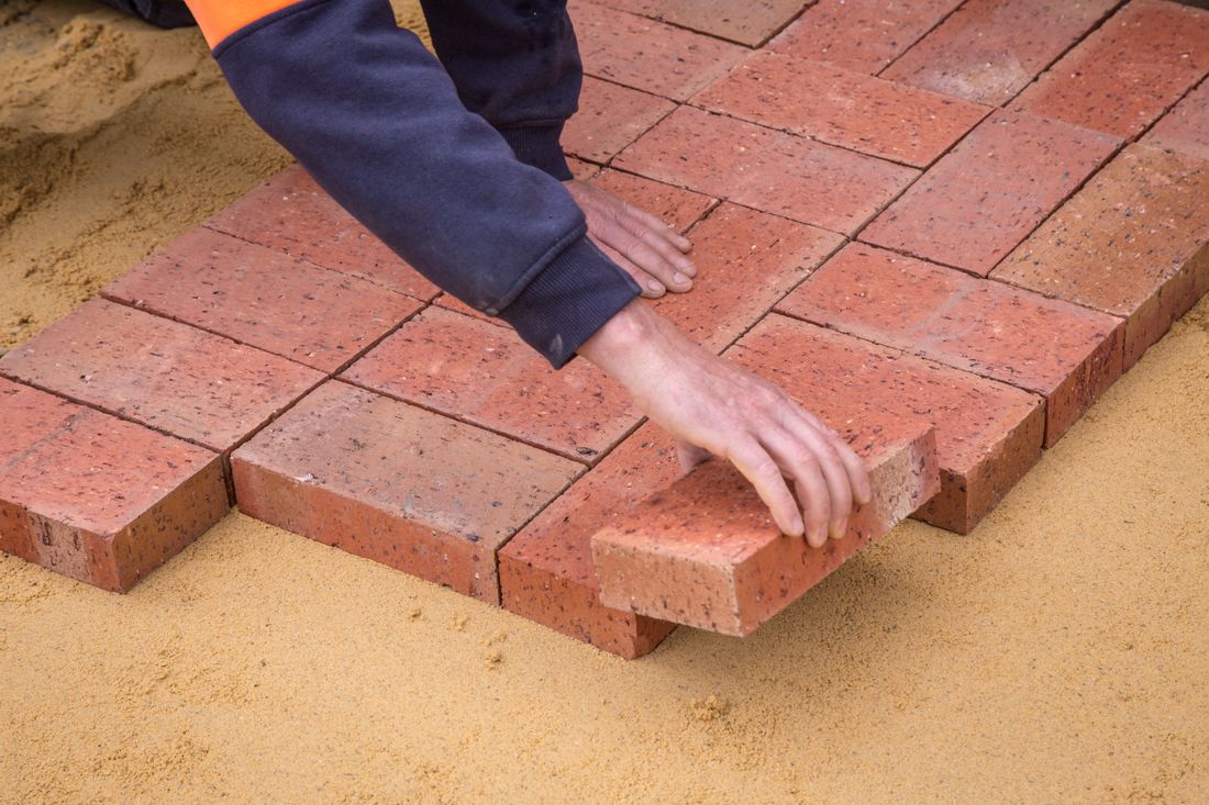 Hands laying clay block paving on a prepared sand bed
