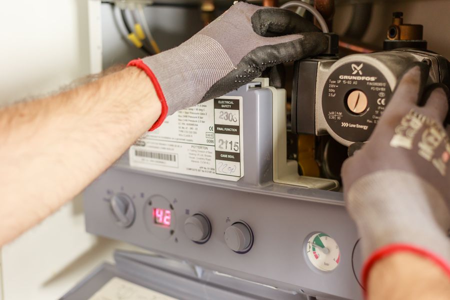 Gloved hands servicing a domestic boiler with its front cover removed